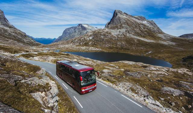 A bus driving next to a lake on a sunny day in Northwest