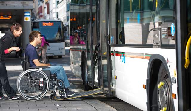 En mann i rullestol får hjelp til å komme seg inn på en buss