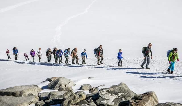 En grupp människor fastspända med säkerhetslina medan de går över en glaciär på väg till Galdhøpiggen i Jotunheimen