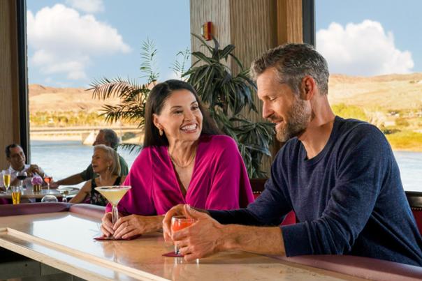 A couple enjoying some delicious cocktails in Laughlin with the beautiful Colorado river behind them.