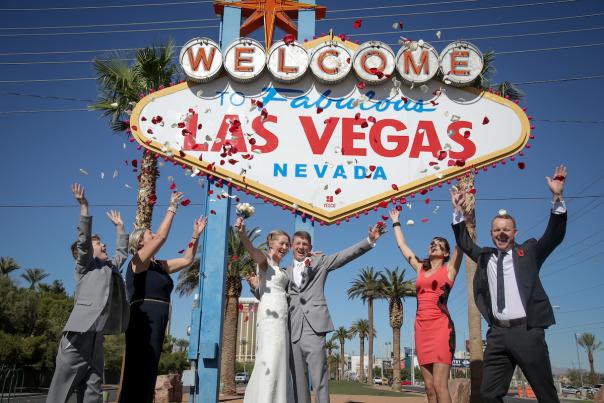 A group celebrating a wedding outside of the famous Las Vegas sign.