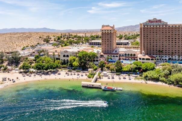 Aerial view of Harrah's Laughlin resort on the Colorado River with a sandy beach, pool area, and jet skier in turquoise water.