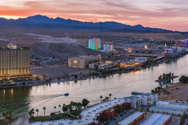 Aerial sunset view of the Colorado River lined with Laughlin casino resorts, mountains, and desert terrain.