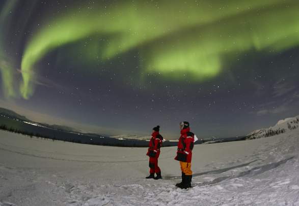 Two people standing under the northern lights in Lyngenfjord
