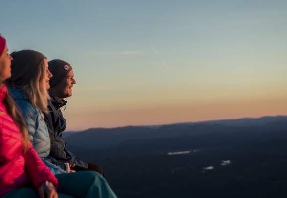 Three people are sitting and enjoying the view from Mount Gaustatoppen in Telemark, Eastern Norway at dusk.