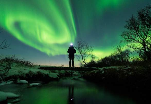 A person standing close to a lake in Varanger surrounded by northern lights