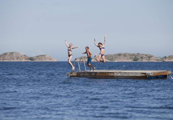 Three kids jumping off a floating pier in Grimstad in Southern Norway.