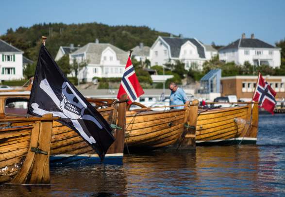 Wooden boats, one with a pirate flag, in Farsund, Southern Norway on a summer day.