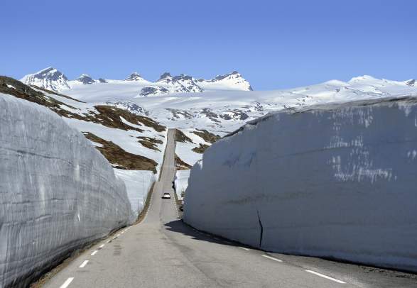 A car between large snow banks on Norwegian Scenic Route Sognefjellet, Fjord Norway