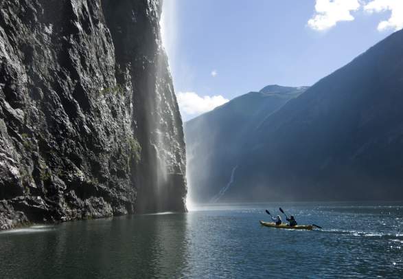 A man and a woman paddling close to a waterfall in the Geirangerfjord