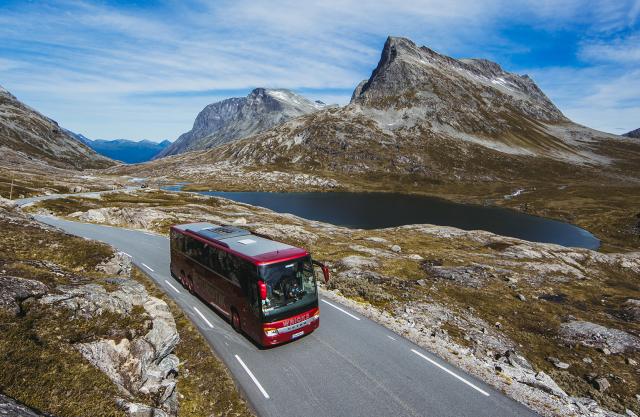 A bus driving next to a lake on a sunny day in Northwest