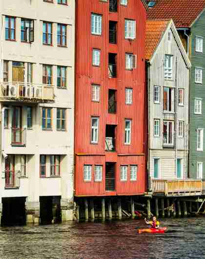 People kayaking on the Nidelven river with old wooden houses in the background. Trondheim, Norway