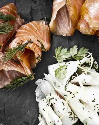 A stone platter with smoked salmon and other food