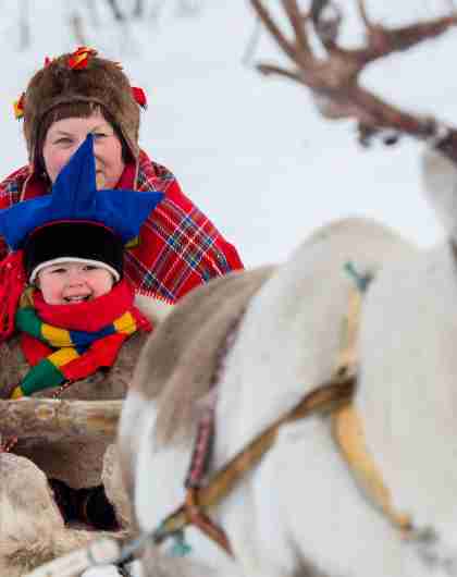 A woman and a little boy riding a reindeer sledge in Finnmark in Northern Norway
