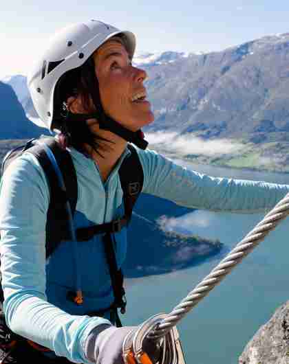 A woman climbing a mountainside on a sunny day in Loen