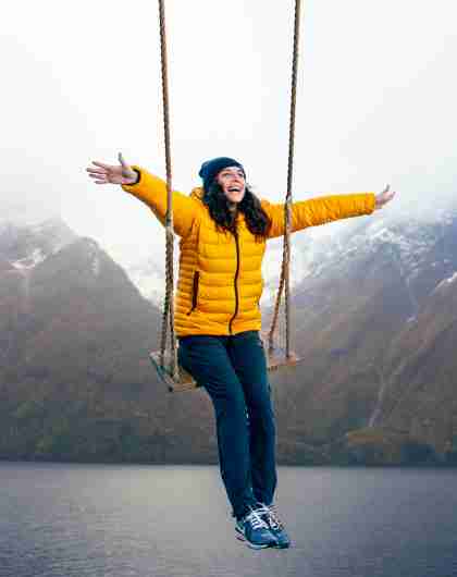 A person on a swing with views of snow-clad mountains and the Hjørundfjord in Fjord Norway