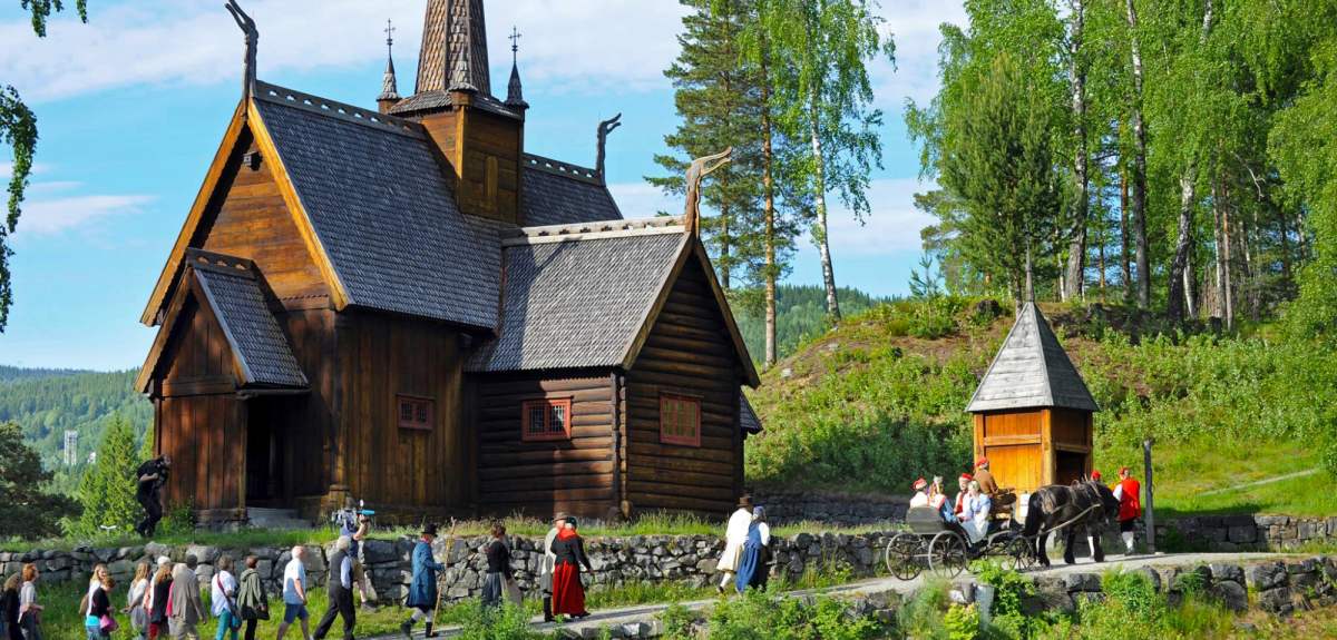 A group of people in old costumes walk past the stave church at Maihaugen in Lillehammer, Eastern Norway