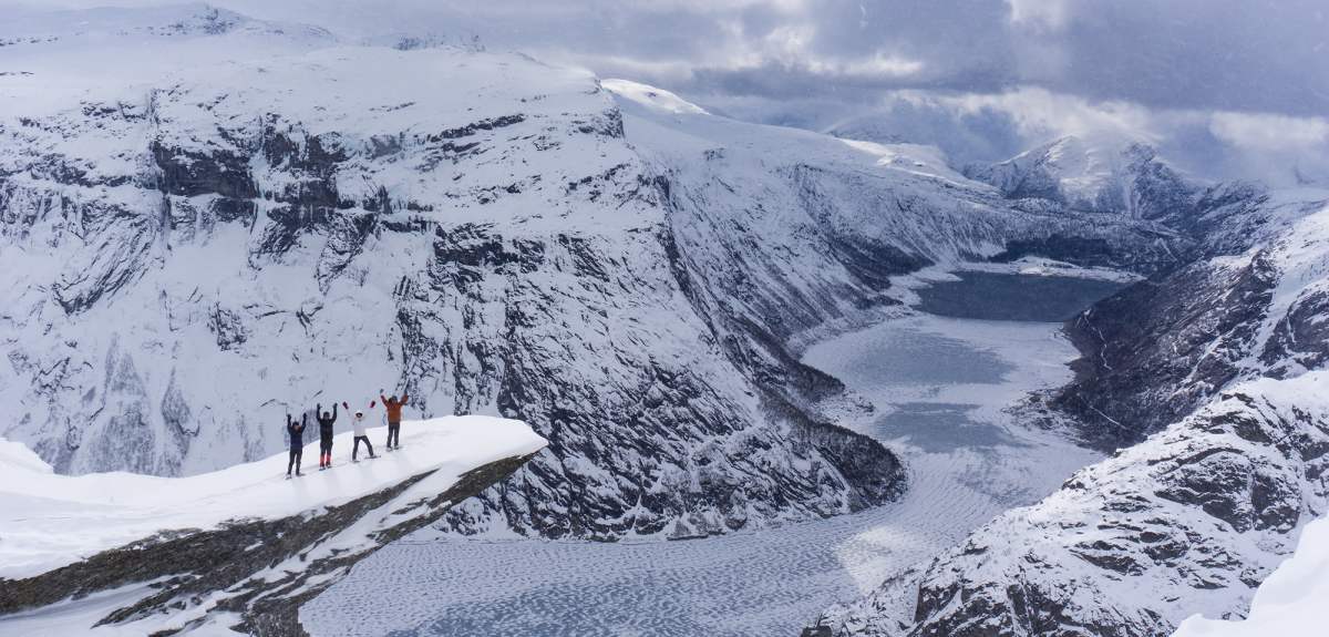 Un grupo de cuatro personas con raquetas de nieve disfruta las vistas desde lo alto de Trolltunga, en la Noruega de los fiordos, en un día de invierno.