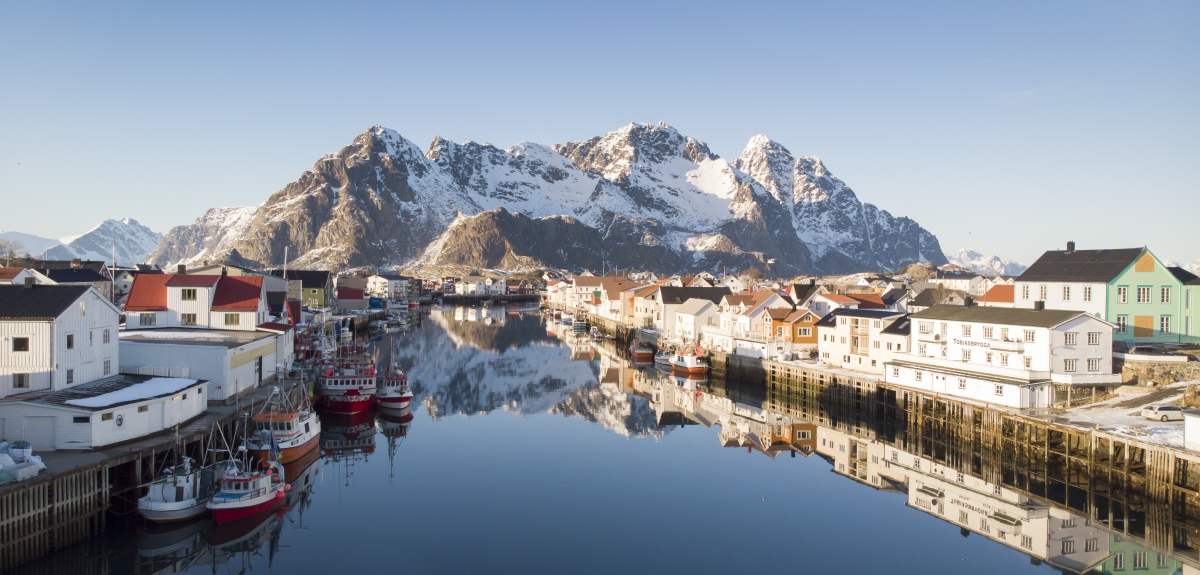 Wooden houses, fishing boats and snowcapped mountains, Henningsvær in certified Sustainable Destination Lofoten, Northern Norway