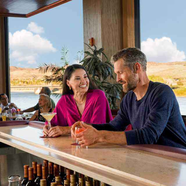A couple enjoying some delicious cocktails in Laughlin with the beautiful Colorado river behind them.