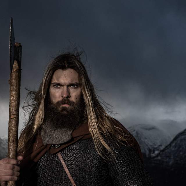 Un hombre con una armadura vikinga se para en un bosque.