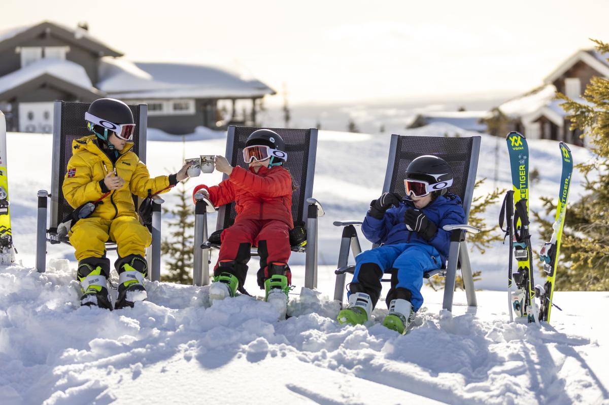 Three children enjoying snacks while taking a break from alpine skiing at one of the family-friendly ski resorts in Norway