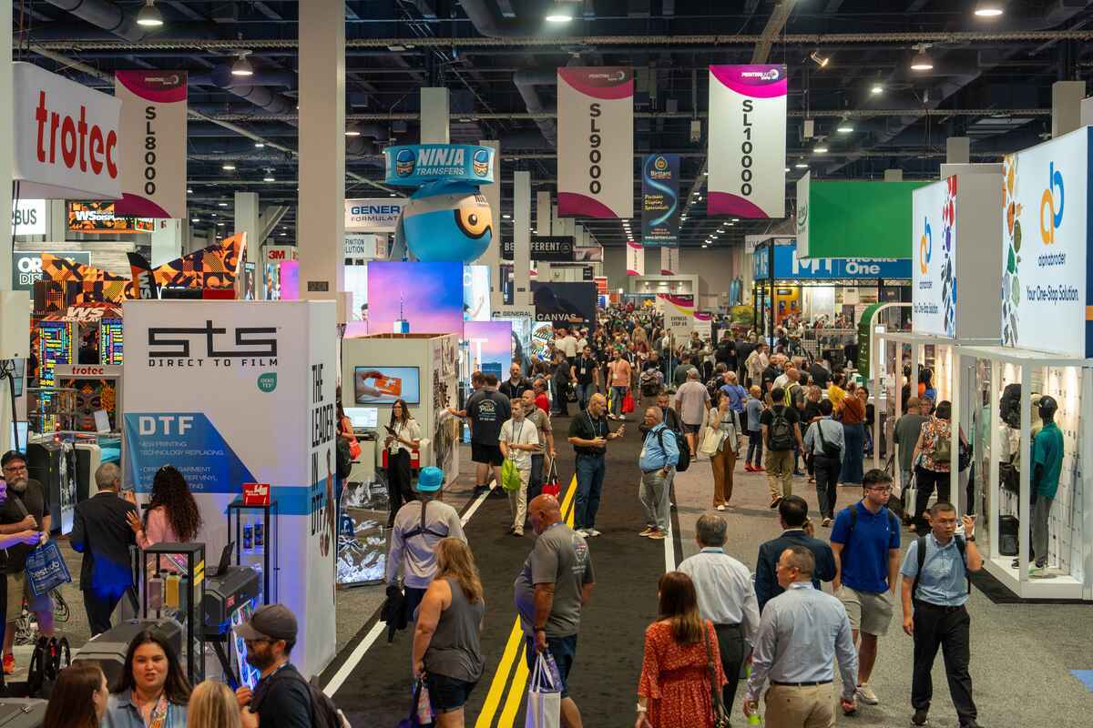 A group of people walking through a printing expo with booths in Las Vegas.