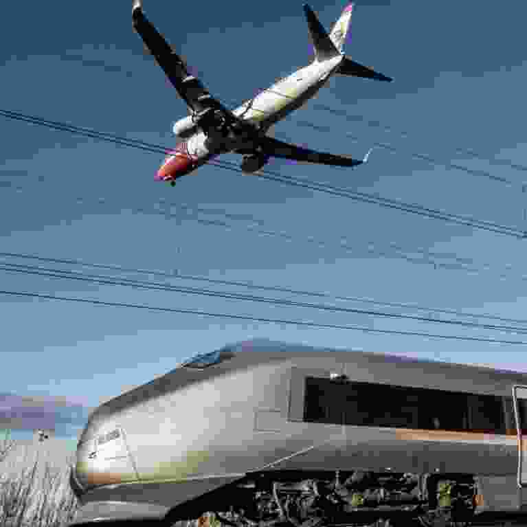 A Norwegian Air shuttle flying over Flytoget Airport Express train outside Oslo
