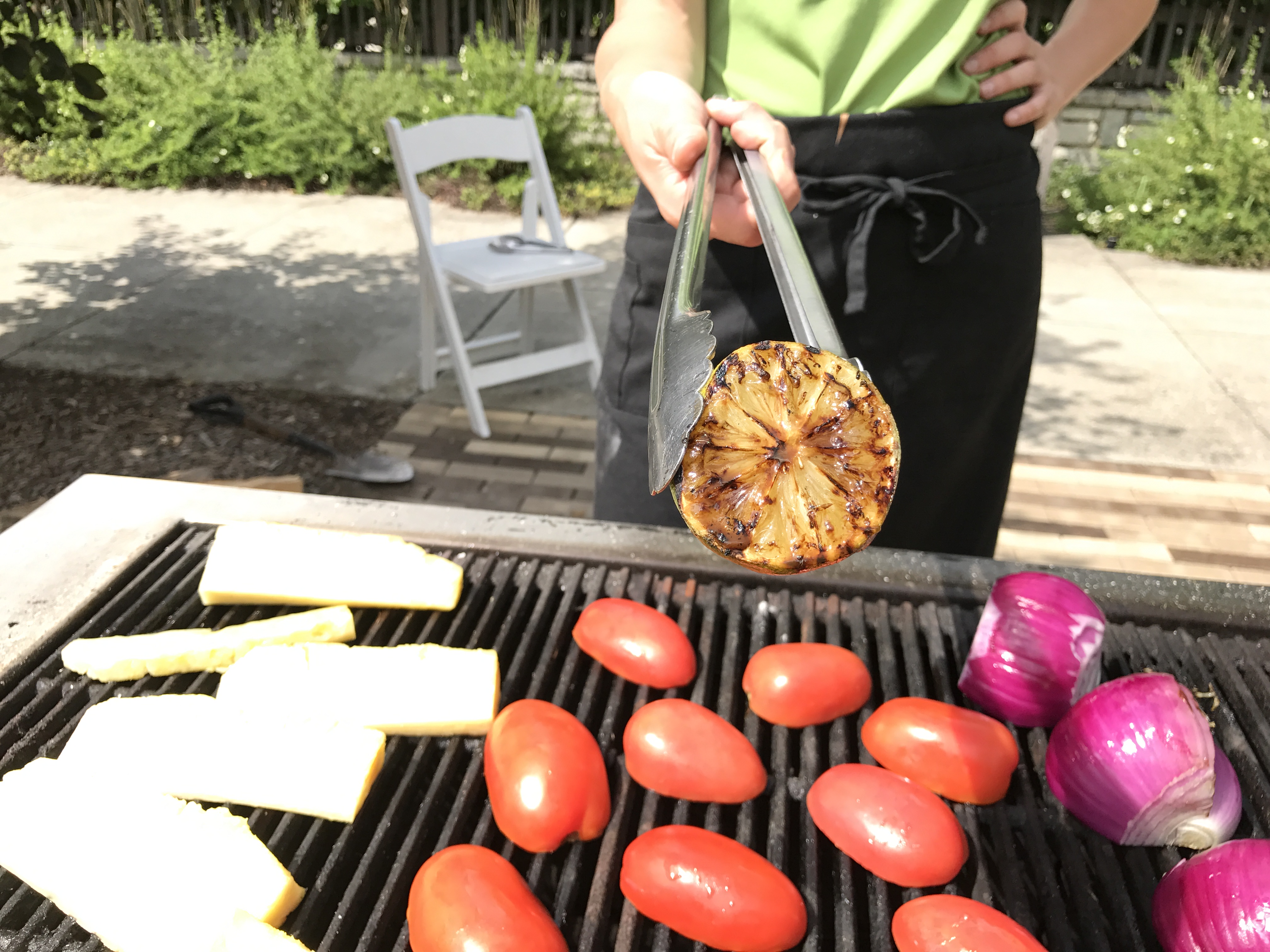 Pineapple, tomatoes and onions on grill outdoors with cooking instructor holding tongs