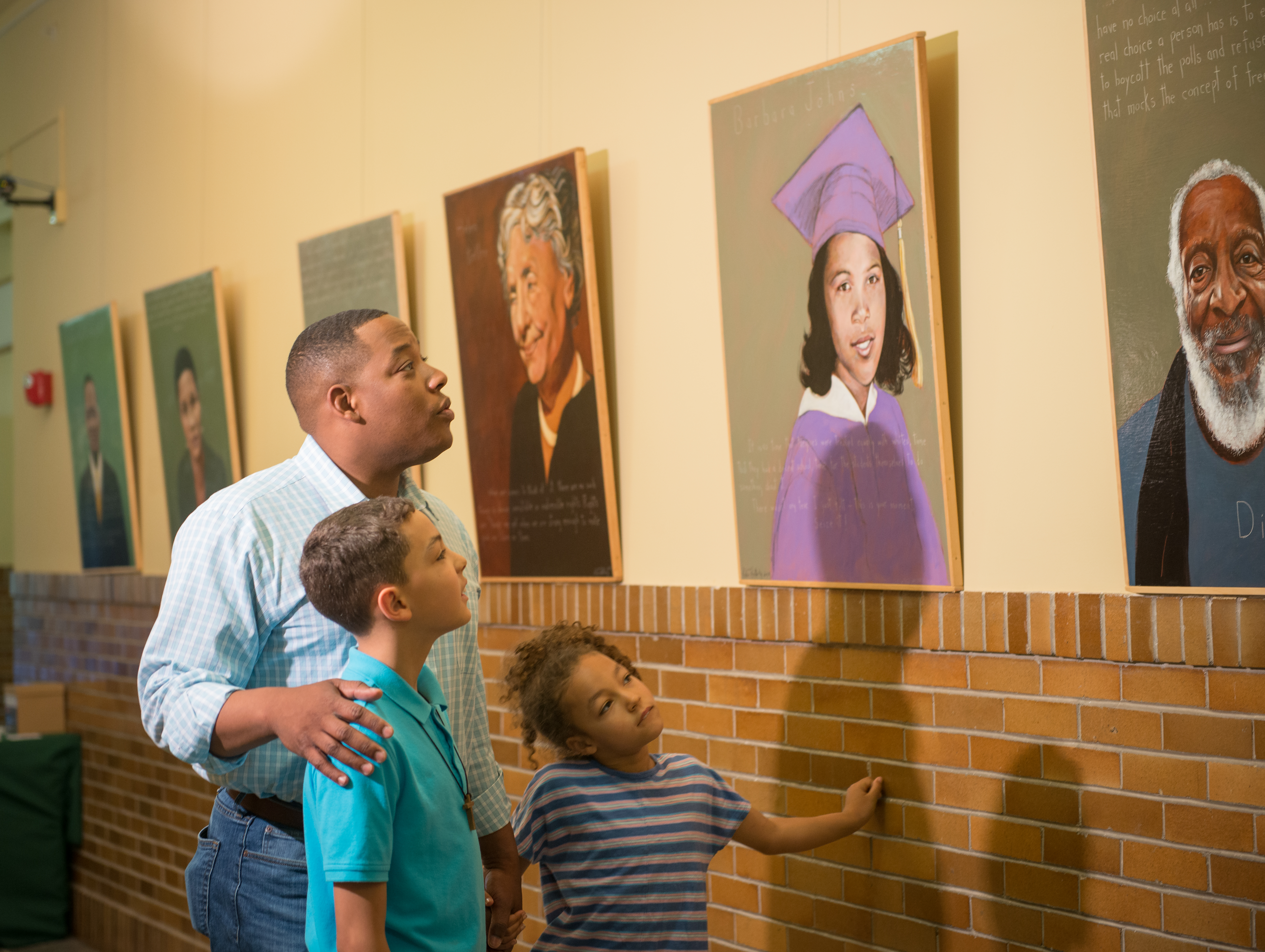 A father and two children admiring portraits at the Brown V Board Museum.