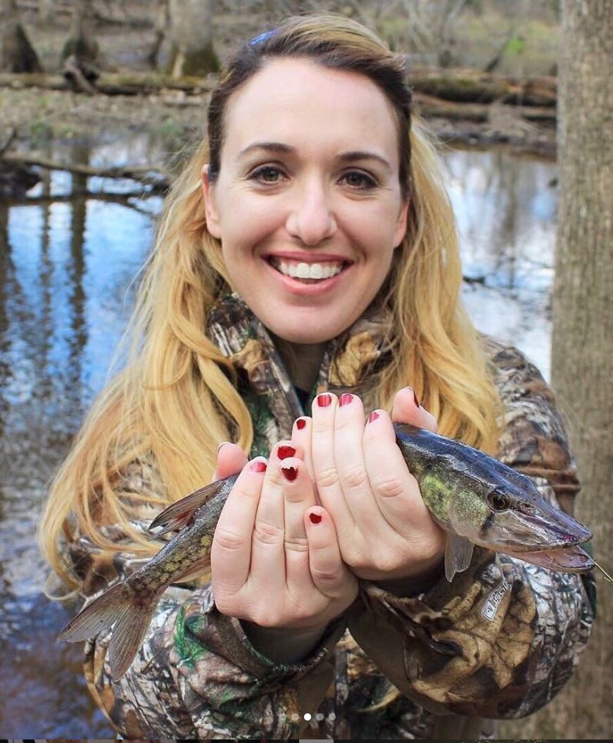 female holding a fish in front of a pond